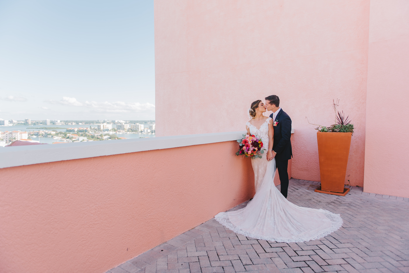 Bride and Groom Portrait at Clearwater Wedding Venue Hyatt Regency Beach Hotel | Bright Tropical Colorful Wedding Bouquet | Ivory and Champagne Lilian West Sheath Wedding Dress Bridal Gown with V Neck Off The Shoulder Straps, Scalloped Edge Train | Tampa Bay Wedding Photographer Kera Photography
