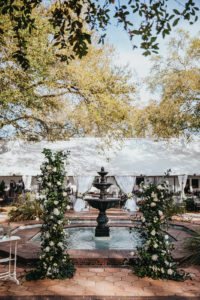 Ybor City Tampa Outdoor Historic Museum Garden Wedding Ceremony with Fountain Backdrop | Wedding Ceremony Backdrop Floral Arrangements with Classic White Roses and Lisianthus and Natural Greenery by Tampa Wedding Florist Monarch Events and Designs