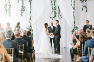 Florida Bride and Groom Exchanging Wedding Vows During Ceremony | White Linen Draping with Lush Greenery Garland and Arrangements | Tampa Bay Wedding Photographer Kera Photography | Tampa Bay Wedding Planner Breezin' Weddings | Historic Wedding Venue The Orlo