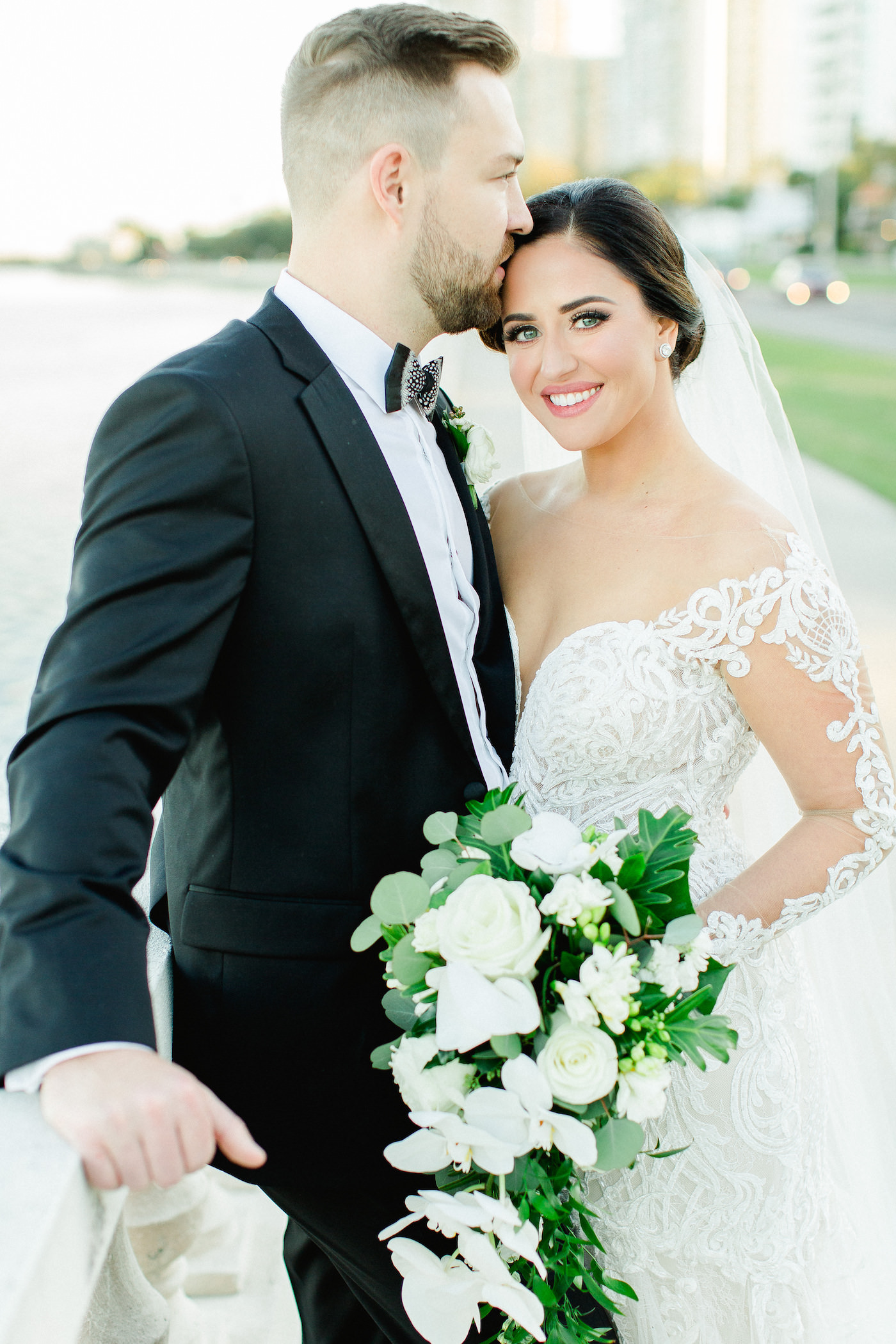 Classic Tampa Bay Bride and Groom Wedding Portrait on Bayshore Boulevard, Florida Bride in Illusion Lace Sleeve Fit and Flare Wedding Dress, Holding Wedding Floral Bouquet with White Orchids, Ivory Roses and Greenery