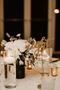 Gold Script Table Number | Gold Votive Candles and White Floral Centerpiece of Ivory Roses Chrysanthemums Lillies and Orchids and Floating Candles