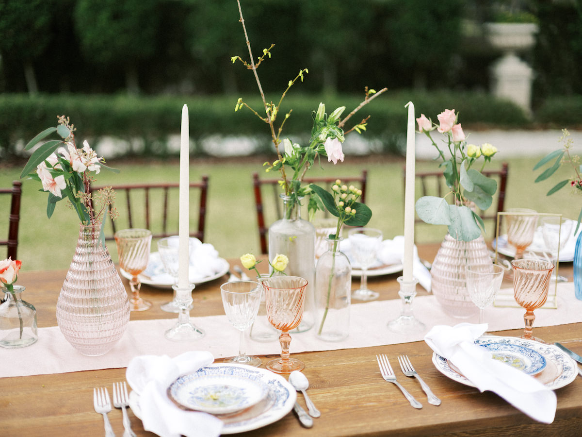 Wood Feasting Table Centerpiece Decor with Bottles and Bud Vases and Candlesticks | Vintage Mismatched China Place Settings with Pink Colored Glassware | Tampa Styled Shoot European Pastel Spring Wedding Inspiration