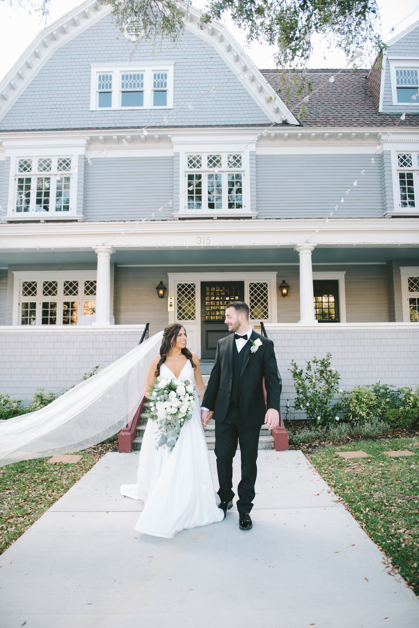 Romantic Classic Bride and Groom Outside Historic Wedding Venue The Orlo | Bride in Full Length Veil Holding Lush Greenery and White Floral Bouquet, Groom in Classic Black Tuxedo | Tampa Bay Wedding Photographer Kera Photography