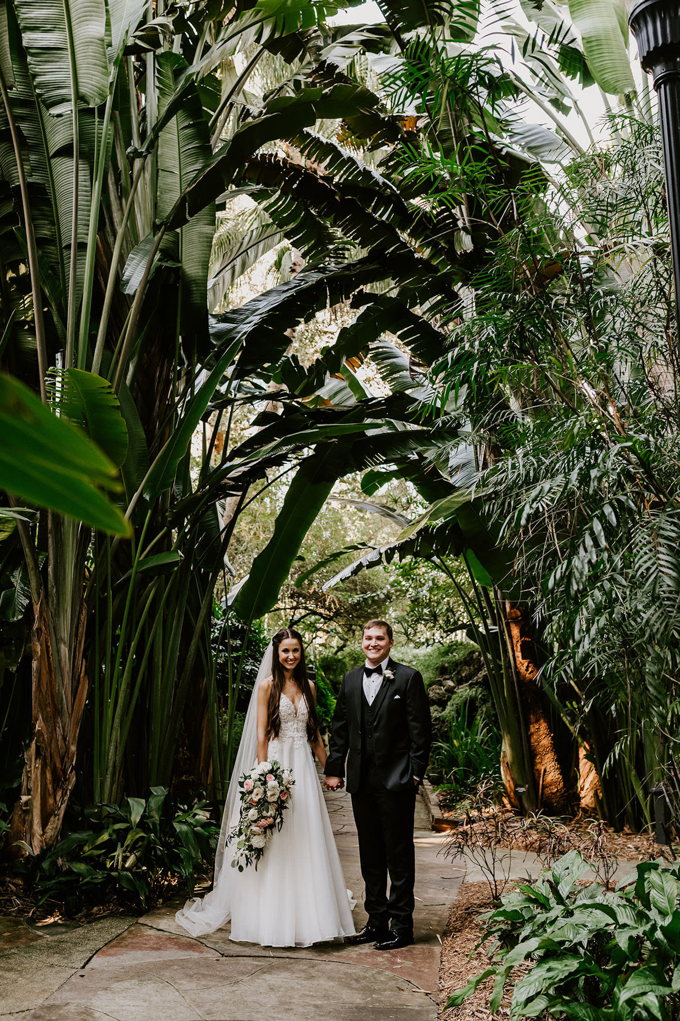 Bride and Groom Outdoor Garden Wedding Portraits | St. Pete Wedding | Lace and Organza Wedding Dress Bridal Gown with Cathedral Veil | Groom in Classic Black Tuxedo Suit with Bow Tie