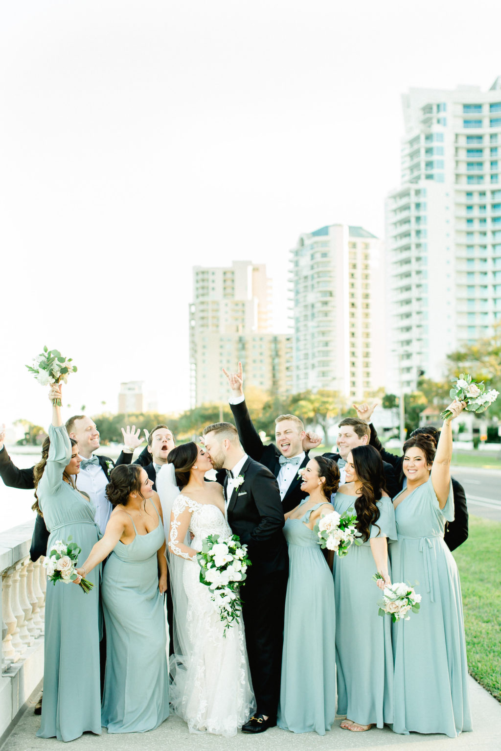 Tampa Bay Fun Wedding Party on Bayshore Boulevard, Bridesmaids in Long Mix and Match Show Me Your Mumu Dresses, Florida Bride in Illusion Lace Sleeve Fit and Flare Wedding Dress, Holding Wedding Floral Bouquet with White Orchids, Ivory Roses and Greenery | Florida Wedding Planner Breezin' Weddings