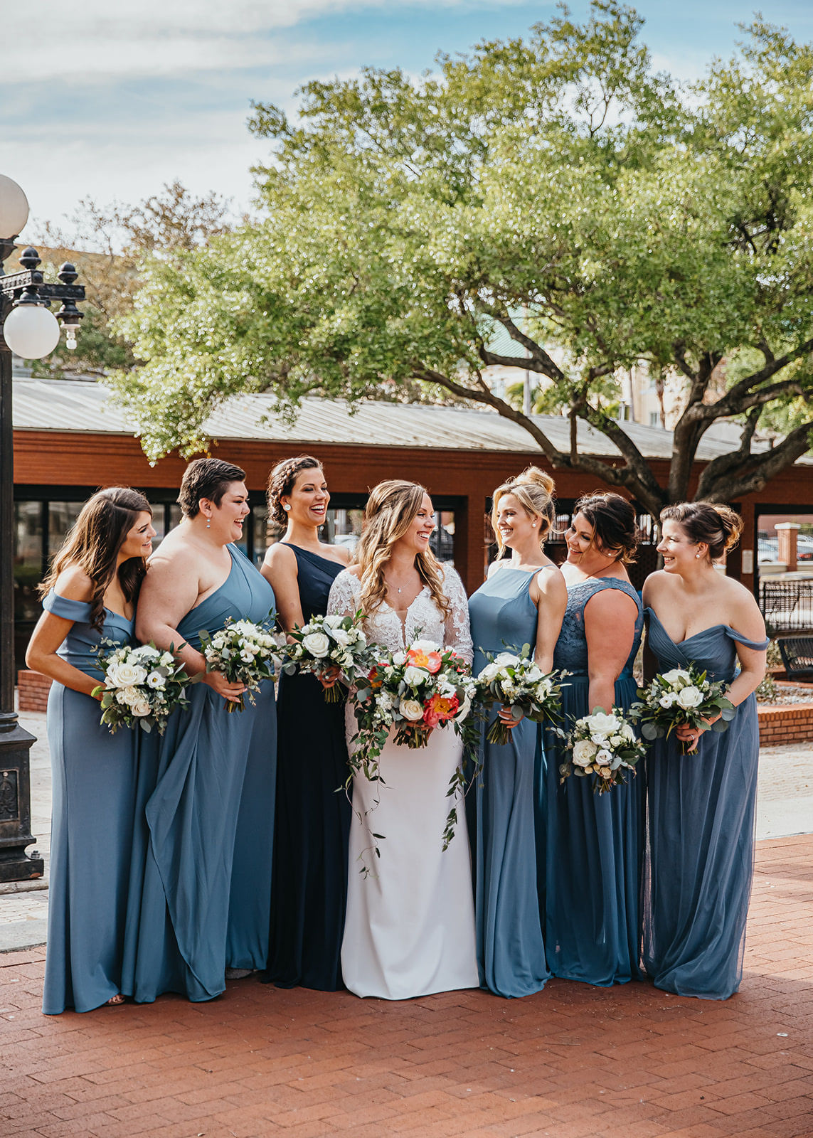 Bride and Bridesmaids Outdoor Portrait Shot | Steel Grey Dusty Blue Long Chiffon Bridesmaid Dresses by David's Bridal | Long Sleeve Lace V Neck Bridal Gown Wedding Dress | Classic White Rose and Greenery Bridesmaid Bouquets with Coral Peonies in Bridal Bouquet | Tampa Wedding Florist Monarch Events and Designs