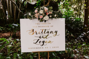 St. Pete Wedding Welcome Sign with Gold Foil Calligraphy on Acrylic on a Gold Easel with Blush Pink and White Roses and Greenery Floral Arrangement