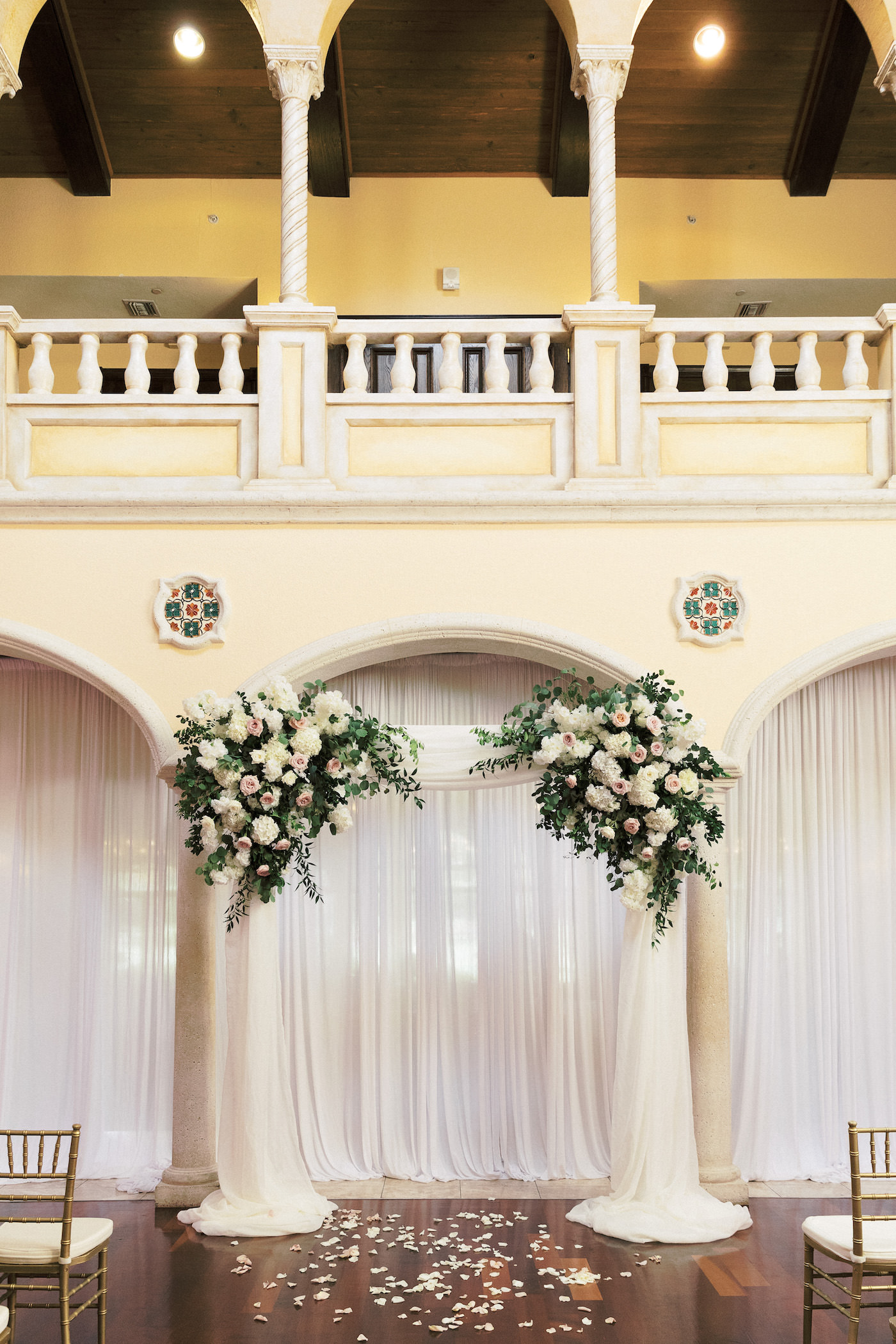 Tampa Wedding Venue Avila Golf & Country Club Indoor Ceremony with Gold Chiavari Chairs, Pipe and Drape Backdrop with Blush Pink and Ivory Rose Floral Arrangements with Eucalyptus Greenery