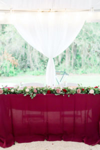 Bride and Groom Outdoor Sweetheart Table with Burgundy Table Linen and Rose and Eucalyptus Greenery Garland