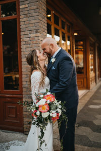 Ybor City Tampa Wedding Bride and Groom Outdoor Portrait | Long Sleeve Lace Bridal Gown Wedding Dress | Classic Navy Blue Groom Suit | Organic Natural Loose Wedding Bridal Bouquet with Coral Pink Peonies and White Roses with Succulents and Eucalyptus Greenery by Tampa Florida Monarch Events and Designs