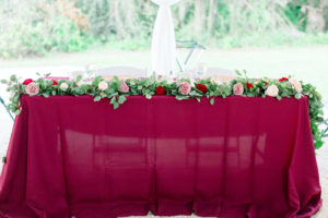 Bride and Groom Outdoor Sweetheart Table with Burgundy Table Linen and Rose and Eucalyptus Greenery Garland