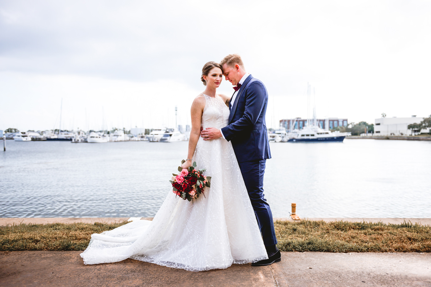 Bride and Groom Outdoor Waterfront Portrait at St. Pete Wedding Venue The Poynter Institute | White Embroidered Organza Ballgown Illusion Neck Bib Neckline Bridal Gown | Groom Classic Navy Blue Suit | Tampa Wedding Dress Shop Truly Forever Bridal