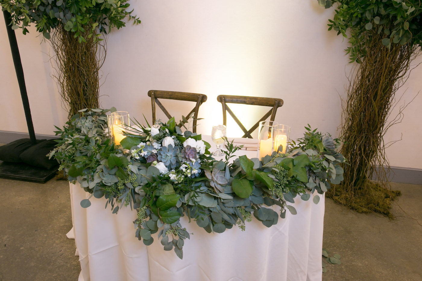 Wes Anderson Inspired Wedding Reception Decor, Eucalyptus, Succulents, White Roses, Greenery Garland on Sweetheart Table with White Linen, Wooden Cross back Chairs, Curly Willow Trees | Wedding Photographer Carrie Wildes Photography | Tampa Bay Wedding Florist Monarch Events and Design | Wedding Planner UNIQUE Weddings and Events