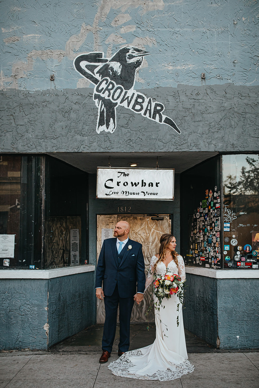 Ybor City Tampa Wedding Bride and Groom Outdoor Urban Bar Portrait | Long Sleeve Lace Bridal Gown Wedding Dress | Classic Navy Blue Groom Suit | Organic Natural Loose Wedding Bridal Bouquet with Coral Pink Peonies and White Roses with Succulents and Eucalyptus Greenery by Tampa Florida Monarch Events and Designs