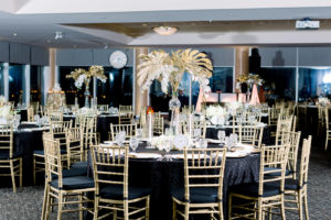 Formal New Year's Eve Wedding Reception Decor, Round Tables with Black Linens, Gold Chiavari Chairs, Tall Vase with Gold Painted Palm Monstera Leaves and White Orchids Centerpieces, White and Gokd Clocks | Wedding Photographer Shauna and Jordon Photography | Tampa Bay Wedding Rentals A Chair Affair | Wedding Planner UNIQUE Weddings + Events
