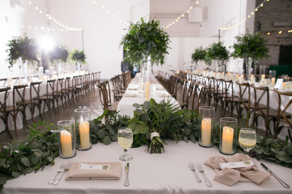 Wes Anderson Inspired Wedding Reception Decor, Eucalyptus Greenery Garland on Sweetheart Table with White Linen, Wooden Cross Back Chairs, Long Feasting Tables | Wedding Photographer Carrie Wildes Photography | Tampa Bay Wedding Florist Monarch Events and Design | Wedding Planner UNIQUE Weddings and Events | Wedding Caterer Olympia Catering