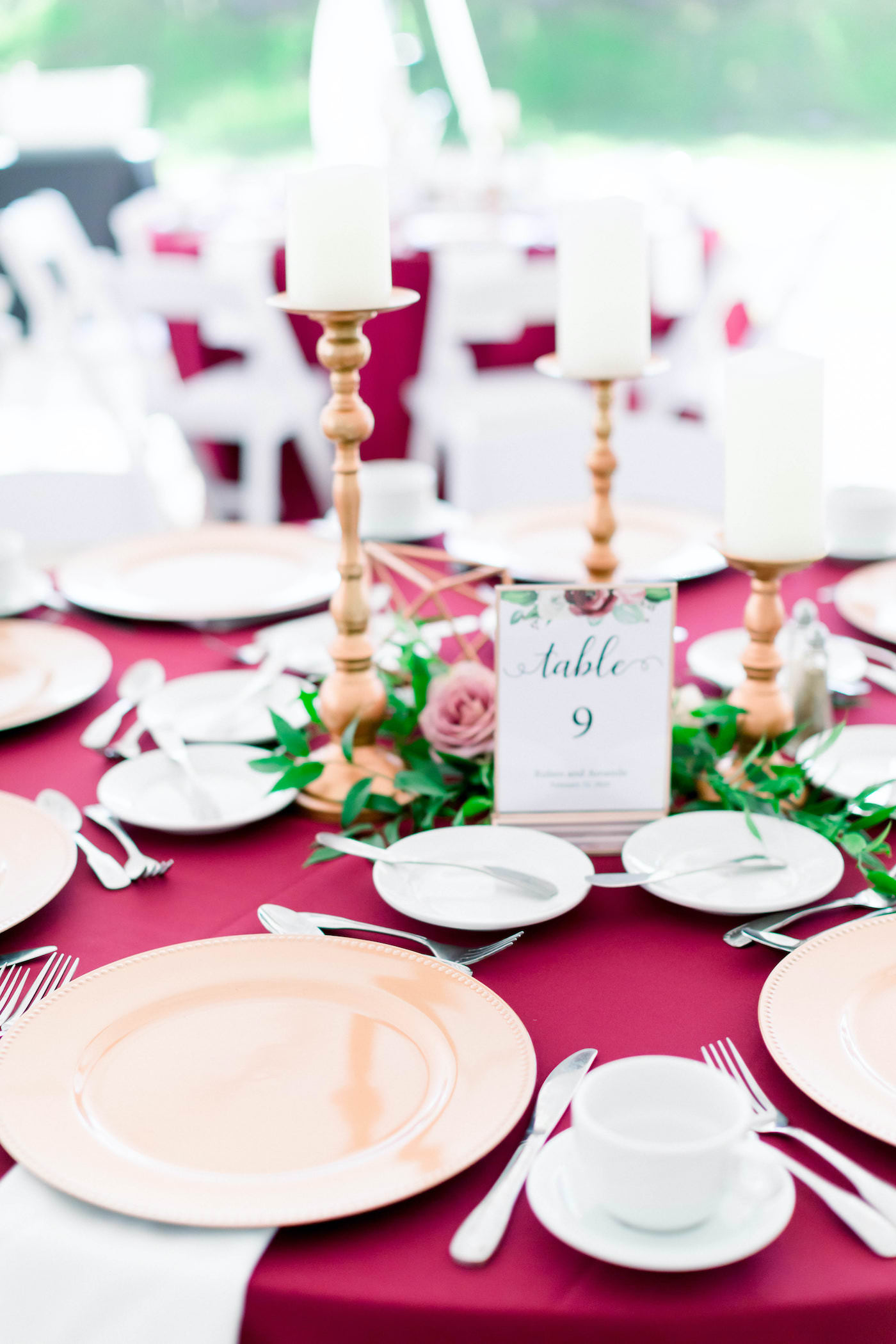 Wedding Reception Table with Burgundy Deep Red Bordeaux Table Linens with Gold Charger Plates and Gold Candlestick Centerpieces accented with Ruscus Greenery