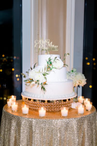 Classic Three Tier White Wedding Cake with Roses and Custom Gold Cake Topper on Table with Gold Sequin Tablecloth and Candles | Wedding Photographer Shauna and Jordon Photography | Tampa Bay Wedding Planner UNIQUE Weddings + Events