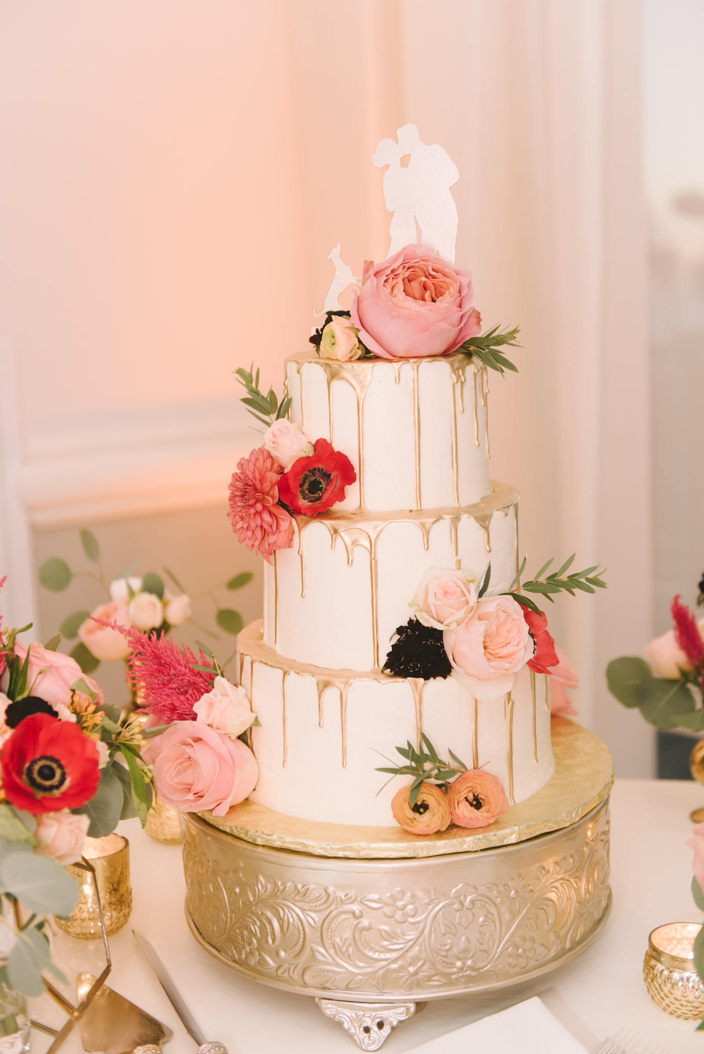 Three Tier Wedding Cake with Dripping Gold Icing and Bright Colorful Fresh Flowers and Custom Silhouette Bride and Groom with Dog Cake Toppers on Round Ornate Gold Cake Stake