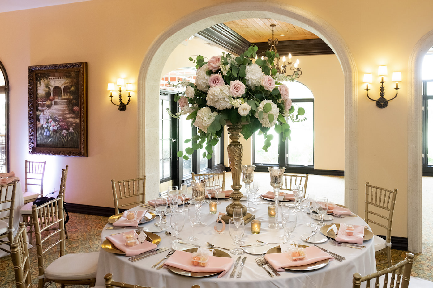 Wedding Reception Table with Gold Chiavari Chairs and Blush Pink Napkins on Gold Charger Plates and Tall Gold Candlestick Loose Floral Centerpiece featuring Blush Pink Roses and Ivory Hydrangea with White Stock and Eucalyptus Greenery | Tampa Wedding Venue Avila Golf & Country Club
