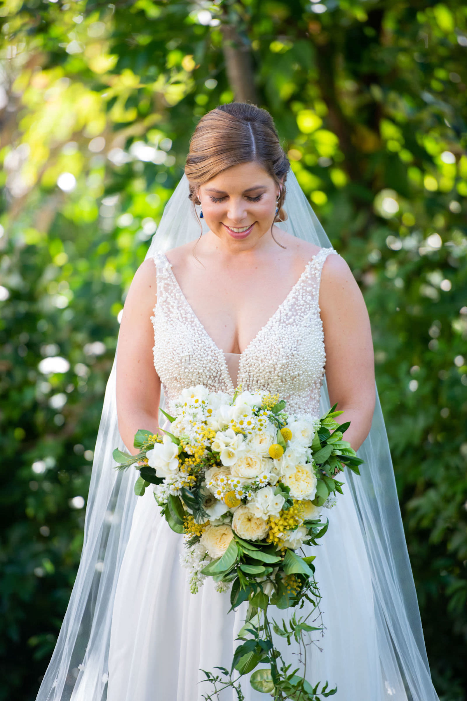 Romantic Bride in Plunging V Neckline Rhinestone Bodice and Flowy Skirt Wedding Dress Holding Garden Whimsicaly Yellow Roses, White and Greenery Floral Bouquet