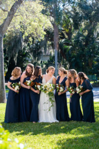 Fun Bride and Bridesmaids in Navy Blue Dresses Holding Garden Inspired White, Yellow and Green Floral Bouquets