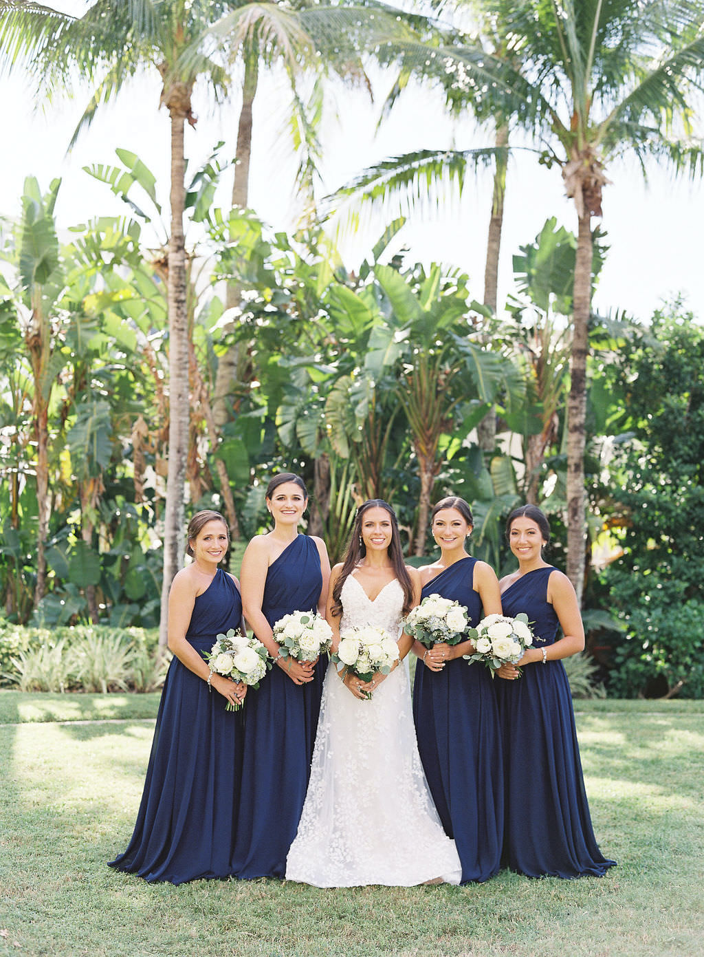Classic Florida Bride and Bridesmaids in Long One Shoulder Navy Blue Dresses, Dark Midnight Blue Brideside Bridesmaid Dresses, Bride Wearing White Lazaro Wedding Dress, Holding Ivory Floral Bouquets with Greenery | Sarasota Luxury Wedding Planner NK Productions Wedding Planning