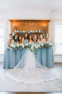 Romantic Classic Bride in Full Length Lace Trim Veil and Bridesmaids in Dusty Blue Mix and Match Dresses Holding Lush White Florals and Greenery Bouquets in Front of Red Brick Fireplace | Tampa Bay Wedding Photographer Kera Photography | Tampa Historic Wedding Venue The Orlo