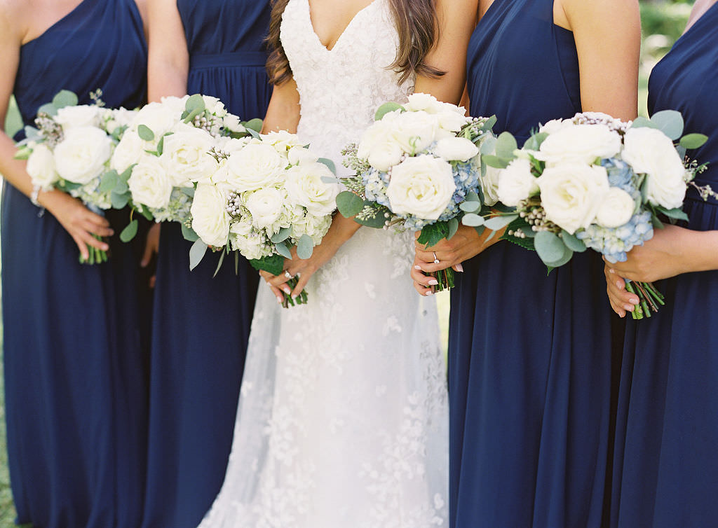 Classic Florida Bride and Bridesmaids in Dark Midnight Blue Brideside Dresses, Bride Wearing White Lazaro Wedding Dress, Holding Ivory and Light Blue Floral Bouquets with Roses and Greenery | Sarasota Luxury Wedding Planner NK Productions Wedding Planning