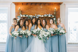 Romantic Classic Bride in Full Length Lace Trim Veil and Bridesmaids in Dusty Blue Mix and Match Dresses Holding Lush White Roses Florals and Greenery Bouquets in Front of Red Brick Fireplace Decorated with Eucalyptus Garland | Tampa Bay Wedding Photographer Kera Photography | Tampa Historic Wedding Venue The Orlo