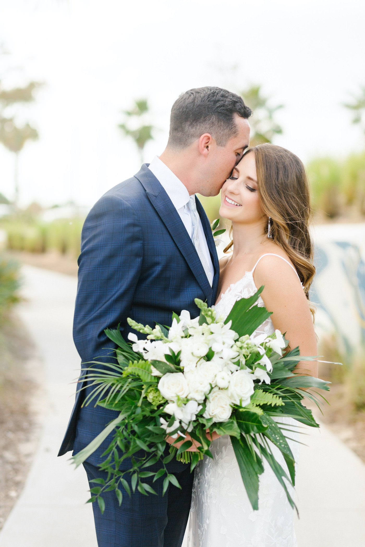 Bride and Groom Outdoor Portrait | Tampa Wedding Florist Bruce Wayne Florals | Florida Tropical Wedding Bridal Bouquet with Greenery Palm Fronds and Ferns and White Roses Orchids and Snapdragons | Groom in Classic Navy Blue Suit