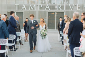 Boho Chic Bride Walking Down the Aisle Holding Lush Greenery and White Roses Floral Bouquet | Waterfront Wedding Venue The Tampa River Center | Wedding Florist Bruce Wayne Florals