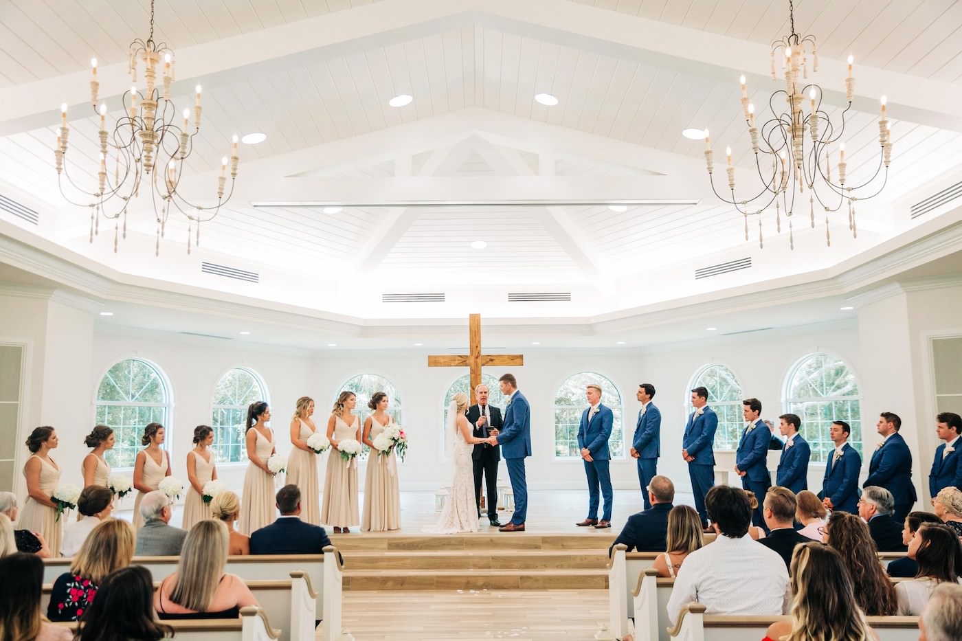 Safety Harbor Wedding Venue Harborside Chapel | Indoor Traditional Church Wedding Ceremony Pews with Cross Backdrop | Nude Champagne Neutral Bridesmaids Dresses with White Hydrangea Bouquets | Navy Blue Groom and Groomsmen Suits