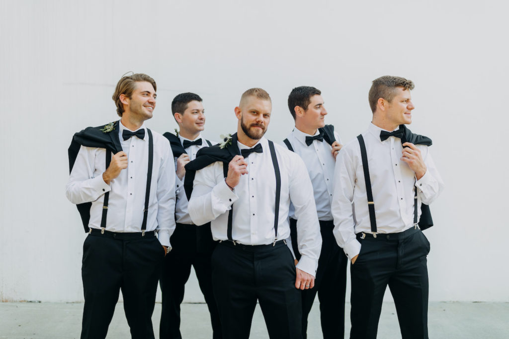 Fun Classic Tampa Bay Groom and Groomsmen in Black Tuxes, Suspenders, Bowties Holding Jackets Portrait | Florida Wedding Planner Blue Skies Weddings and Events