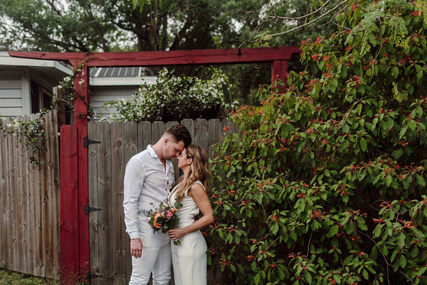Bride and Groom Outdoor Wedding Portrait | COVID Wedding Elopement Backyard Ceremony | Ivory White Bridal Jumpsuit | Casual Groom White Shirt and Pants | DIY Pink and Peach Bouquet with Ranunculus and Eucalyptus Greenery