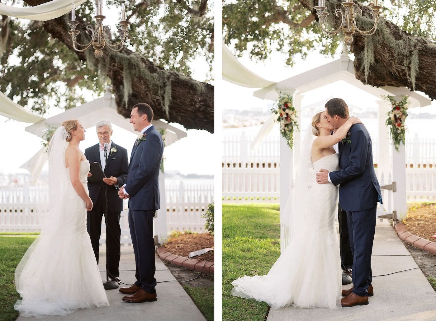 Bride and Groom First Kiss | Florida Fall Autumn Outdoor Waterfront Wedding Ceremony | Strapless Ivory Tulle Rouched Mermaid Vera Wang Bridal Gown with Rhinestone Beaded Sash Waistband | Groom in Classic Navy Blue Suit