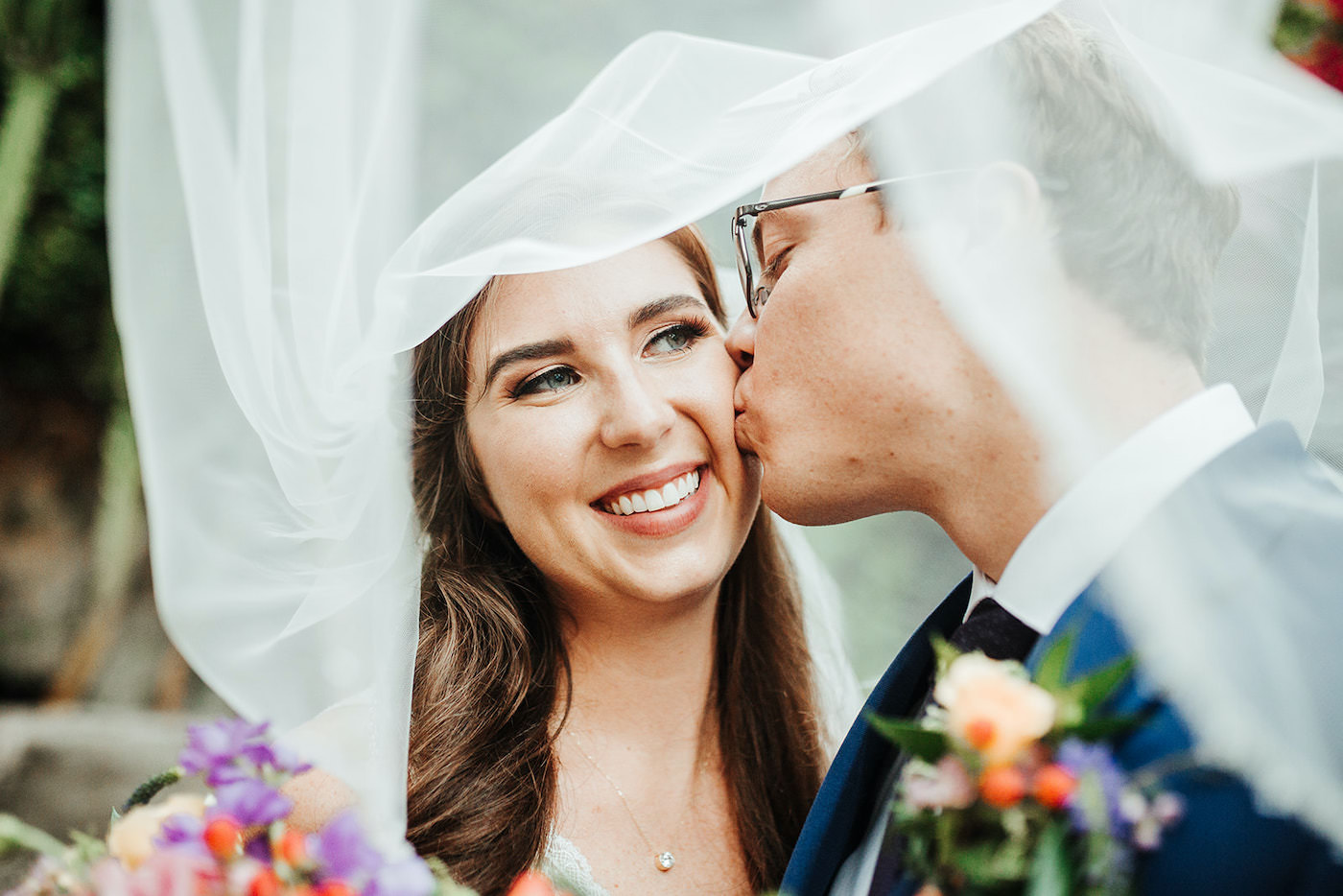 Romantic Groom Kissing Bride on Cheek with Bridal Veil Blowing in Wind Creative Wedding Portrait