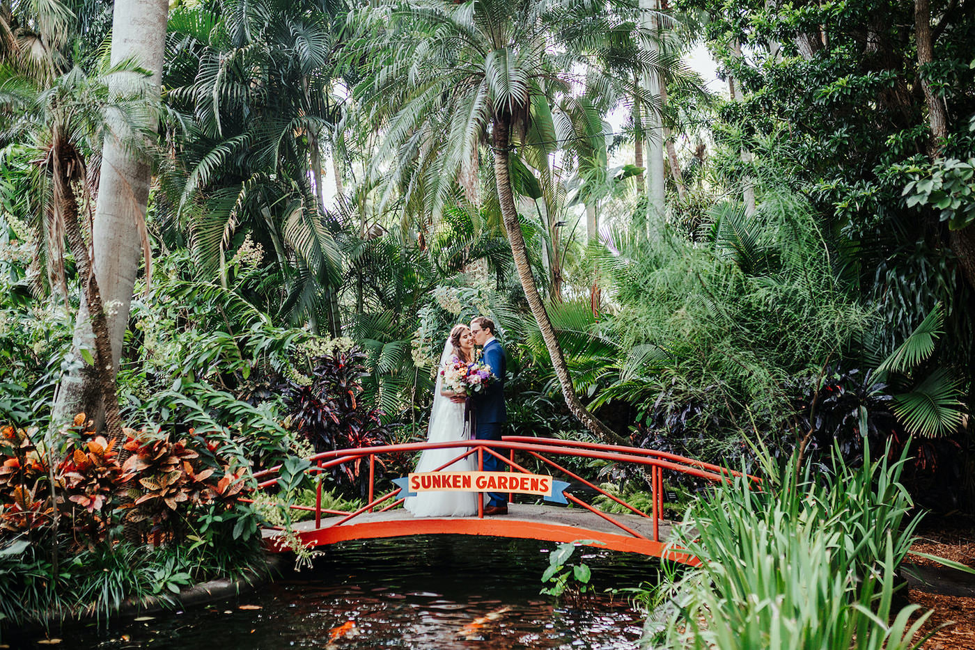 Beautiful Bride and Groom with Tropical Backdrop on Red Bridge at St. Pete Wedding Venue Sunken Gardens | Tampa Wedding Planner Kelly Kennedy Weddings and Events