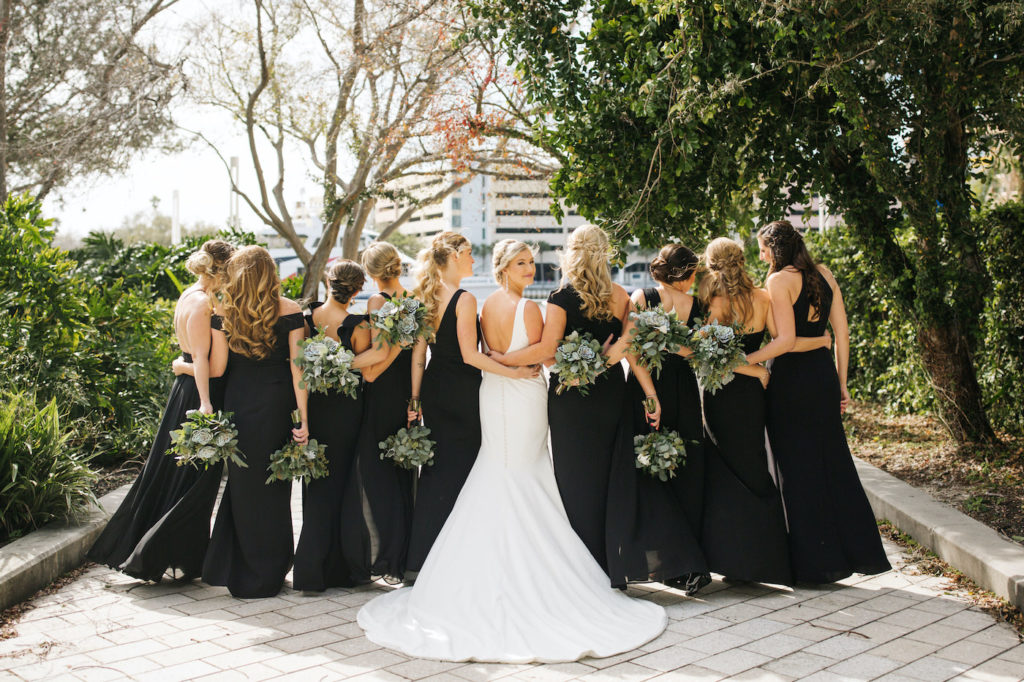 Outdoor Tampa Waterfront Bride and Bridesmaids Portrait | Long Black Mismatched Bridesmaid Dresses | Simple Sheath Ivory Crepe Bateau Neck Bridal Gown by Theia | Natural Loose Greenery Bouquets with Eucalyptus and Succulents and White Roses | Michele Renee the Studio