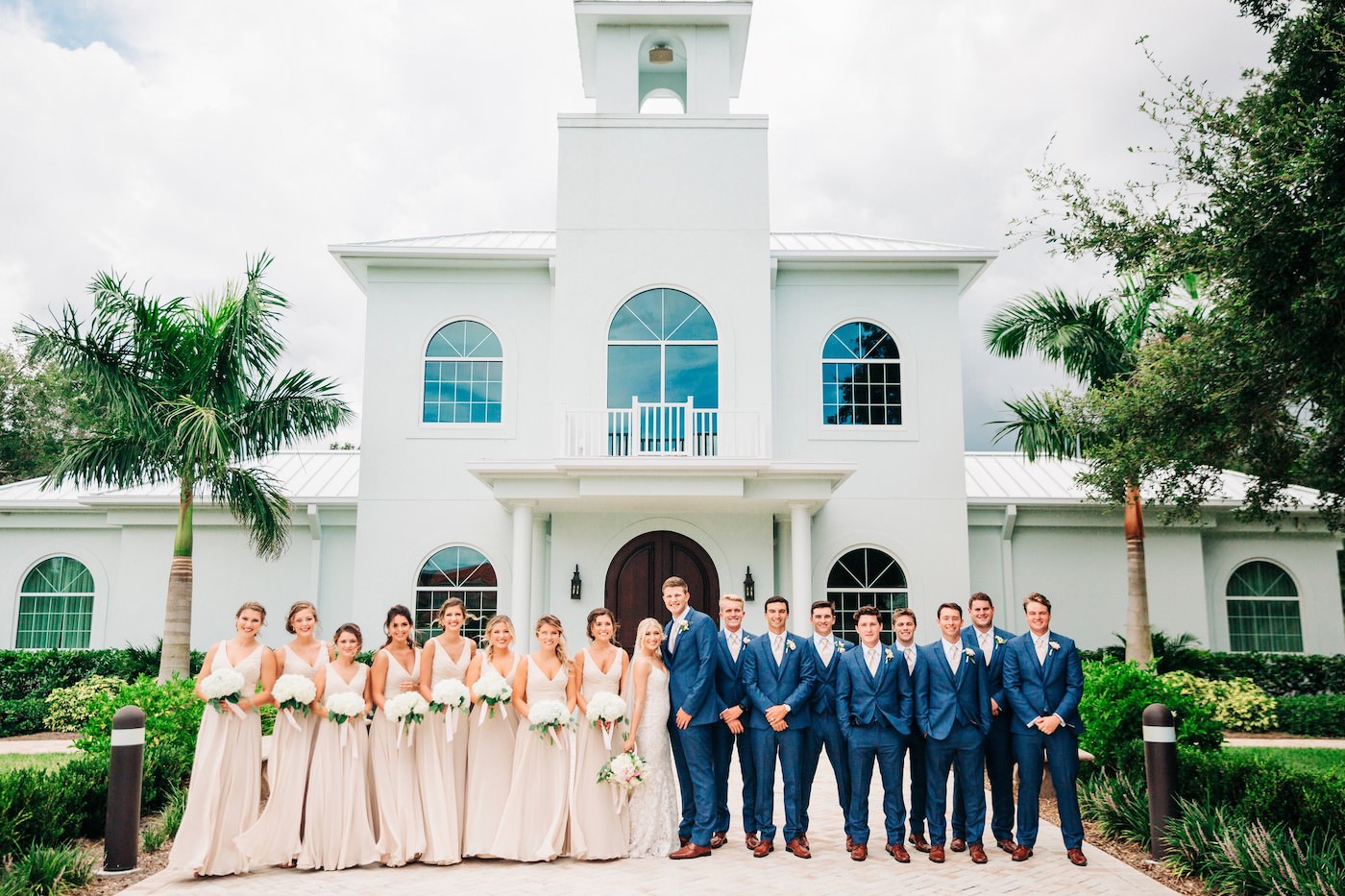 Safety Harbor Wedding Venue Harborside Chapel | Outdoor Wedding Party Portrait at Church Ceremony | Neutral Nude Champagne Watters Bridesmaid Dresses from Bella Bridesmaid | White Hydrangea Bouquets with Cascading Ribbon | Groom and Groomsmen in Navy Blue Suits with Nude Pink Neck Ties