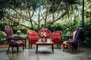 Antique Cocktail Lounge Seating, Red Velvet Love Seat, Purple Velvet Chair and Ivory Chair with Plum Blanket, Wooden Coffee Table with Colorful Floral Arrangement | St. Pete Wedding Venue Sunken Gardens