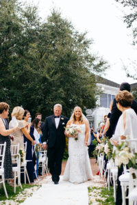 Florida Bride and Father Walk Down the Aisle During Wedding Processional, Bride Wearing Hayley Paige Wedding Dress, Walking on White Aisle Runner Decorated With Scattered Petals | Sarasota Wedding Planner NK Weddings