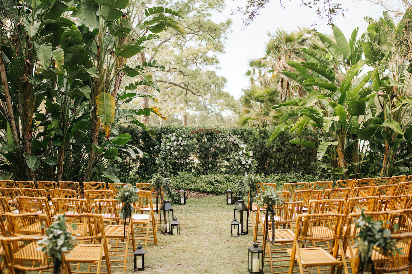 Boho Chic Outdoor Wedding Ceremony at Tampa Garden Club Venue | Natural Wood Bamboo Chairs with Black Lanterns and Eucalyptus Greenery Aisle Markers | Round Wood Moon Arch Ceremony Backdrop with Suspended Geometric Containers and Eucalyptus Greenery Garland Floral Arrangements | Winsor Event Studio