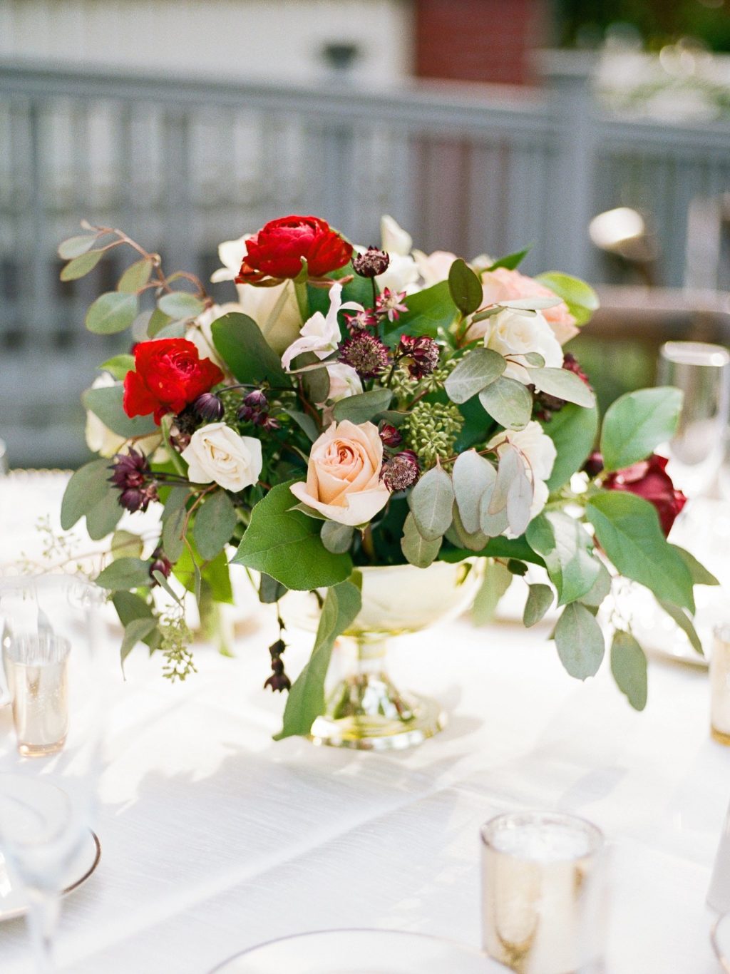 Low Wedding Centerpiece Floral Arrangement of Eucalyptus Greenery, Cream Roses, Red Renunculus, and Bordeaux Chrysanthemums in Gold Pedestal Vase | Tampa Wedding Florist Brides N Blooms