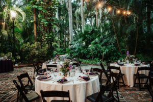 Whimsical Boho Outdoor Courtyard Garden Wedding Reception Decor, Round Tables with Wooden Folding Chairs, Cream Linens, Colorful Floral Centerpieces, Hanging Crystal Chandelier and String Lights | Tampa Bay Wedding Planner Kelly Kennedy Weddings and Events | St. Pete Wedding Venue Sunken Gardens