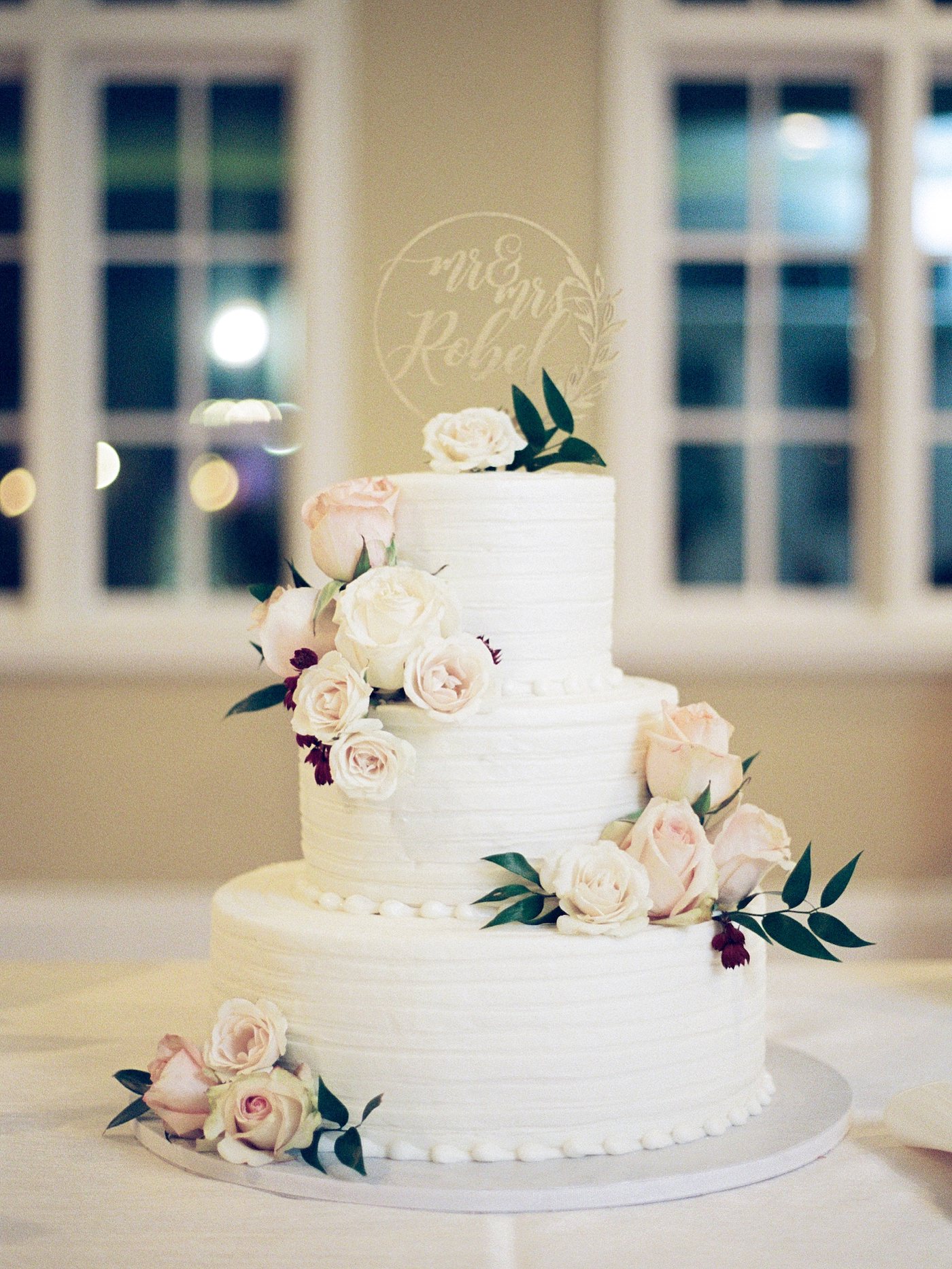 Three Tier Buttercream Wedding Cake with Fresh Flowers and Greenery Accents of Cream Roses and Gold Die Cut Cake Topper