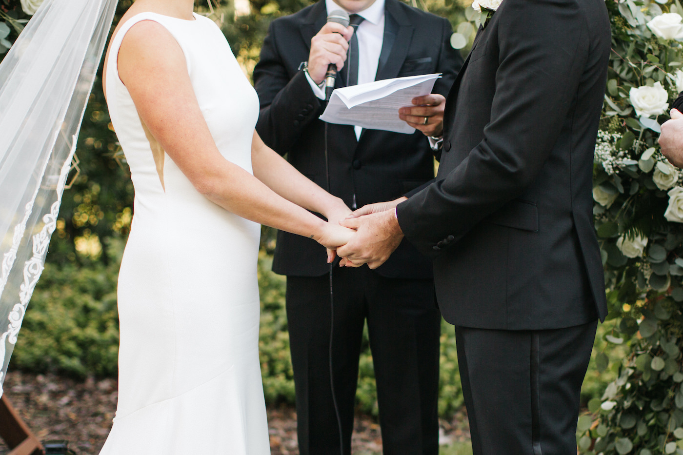 Bride and Groom Holding Hands while Exchanging Vows during Boho Chic Outdoor Wedding Ceremony
