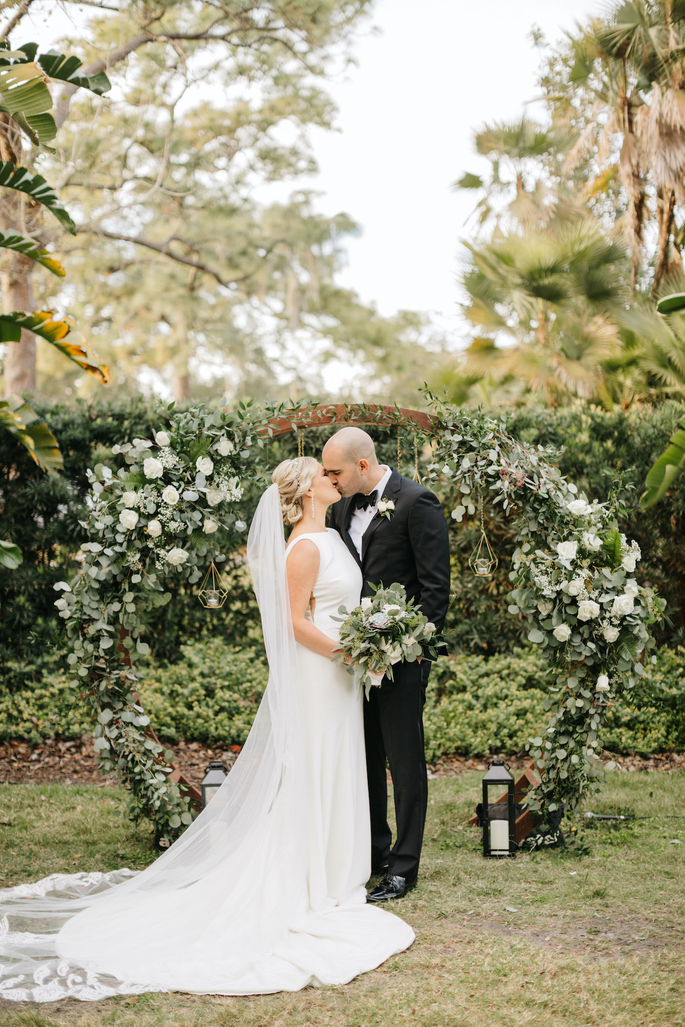 Bride and Groom Outdoor Portrait | Simple Sheath Ivory Crepe Bateau Neck Bridal Gown by Theia | Groom in Classic Black Tux Suit with Bow Tie | Natural Loose Greenery Bridal Bouquet with Eucalyptus and Succulents and White Roses | Boho Chic Outdoor Tampa Wedding Ceremony | Round Wood Moon Arch Ceremony Backdrop with Suspended Geometric Candles and Eucalyptus Greenery Garland with White Rose Floral Arrangements