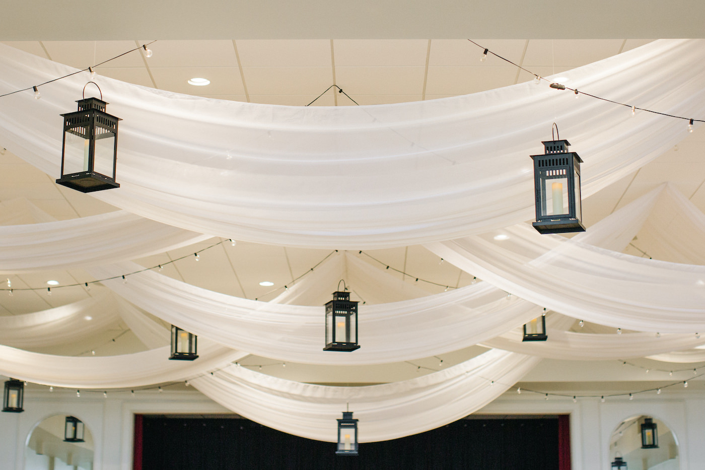 Wedding Ceiling Treatment Installment with Draped Fabric Swags and Canopy Bistro Lights and Suspended Black Lanterns with LED Candles | Tampa Wedding Rentals Gabro Event Services