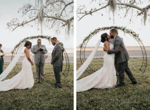 Bride and Groom First Kiss at Outdoor Wedding Ceremony with Metal Round Moon Arch Backdrop with Greenery Garland | Groom in Classic Charcoal Grey Suit | Mori Lee Ivory Lace over Champagne Lining Spaghetti Strap V Neck Mermaid Bridal Gown with Long Cathedral Veil